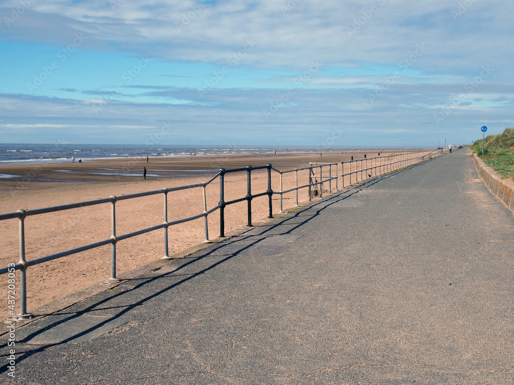 the pedestrian walkway next to the sea in crosby merseyside with distant figures on the beach on summer sunlight