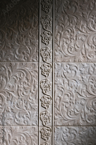 Fragment of textured beige tiles in the bathroom with floral pattern