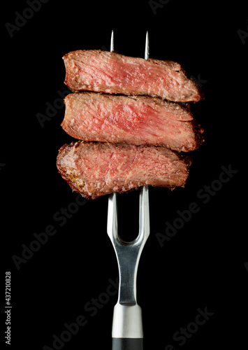 slice of steak on fork at black background