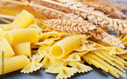 various pasta with ears of wheat on slate background