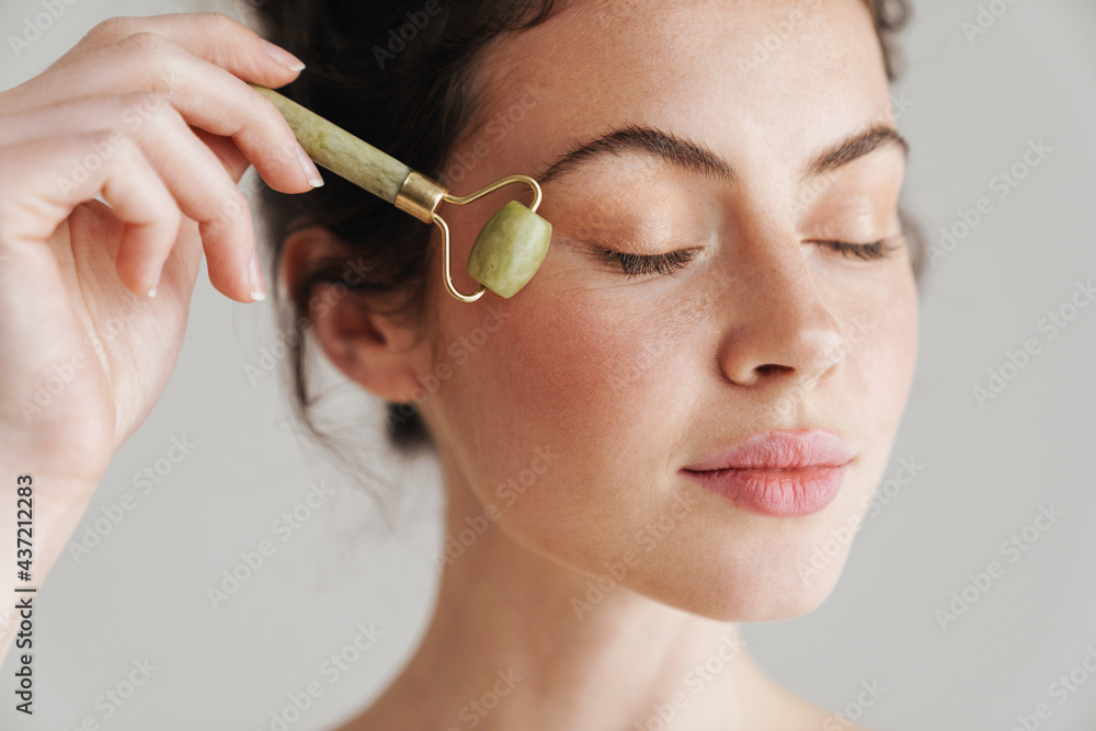 Obraz na płótnie Half-naked brunette woman massaging face with jade roller w salonie