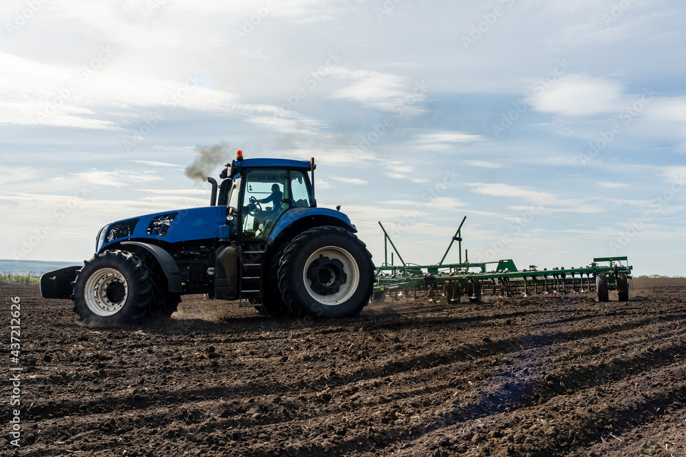 Fototapeta premium A tractor with seedbed cultivator ploughs field on morning.