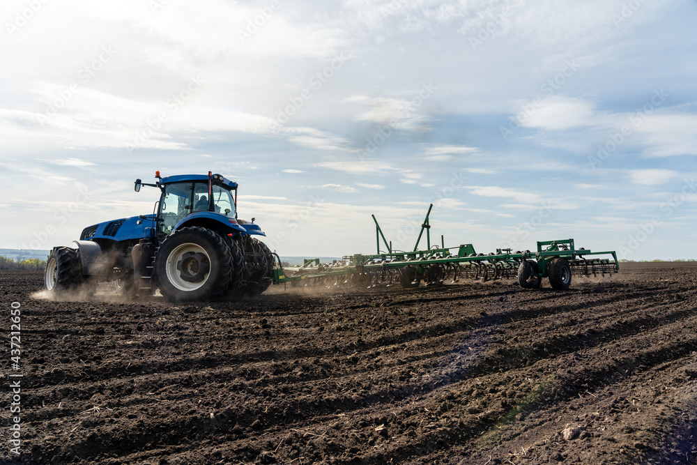 Fototapeta premium A tractor with seedbed cultivator ploughs field on morning.