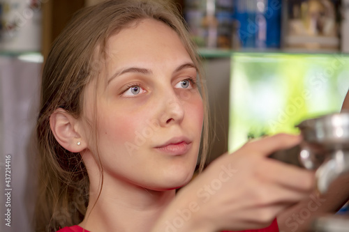 Portrait of a young blue-eyed woman 20-25 years old pouring coffee into a cup from a coffee machine, close-up, selective focus, gaze directed to the side. Concept: Bar work, Post-college employment, L