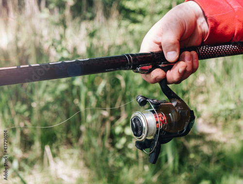 One fisherman holding a fishing rod with a reel in nature, close-up. Fishing concept.