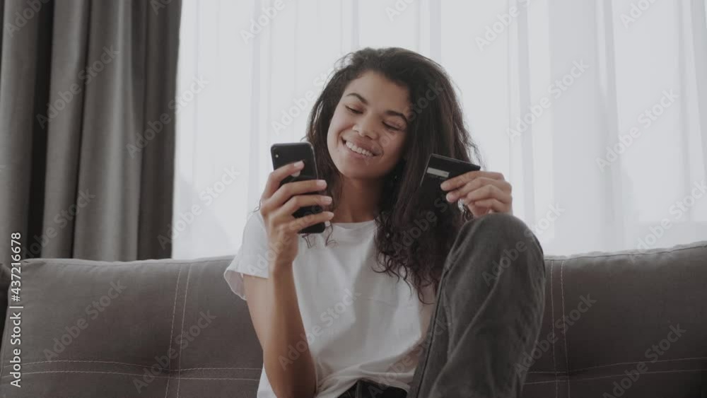 A credit card and smartphone in female hands. Joyful african american young woman looks at the phone screen, shopping online, online payment A credit card and smartphone in female hands. Joyful african american young woman looks at the phone screen, shopping online, online payment