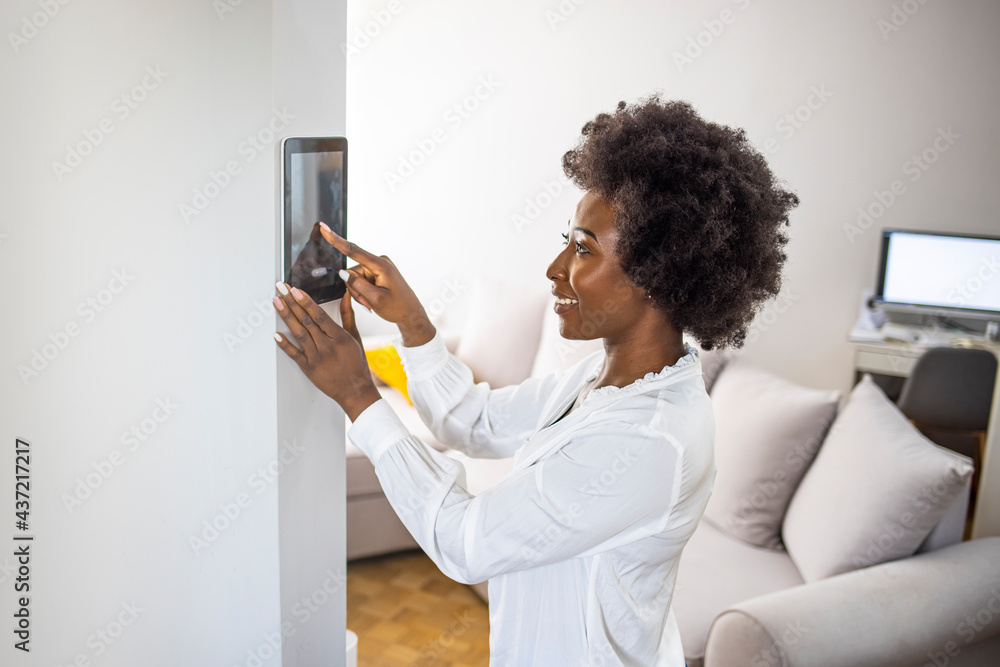 Young african girl woman lady adjusting remote climate control panel settings wall touch screen set heating conditioning switch on security system energy saving mode Young african girl woman lady adjusting remote climate control panel settings wall touch screen set heating conditioning switch on security system energy saving mode