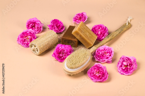 Natural soap, loofah loofah and massage brush on a beige background with roses. Natural organic cosmetics for face and body. Skin care concept