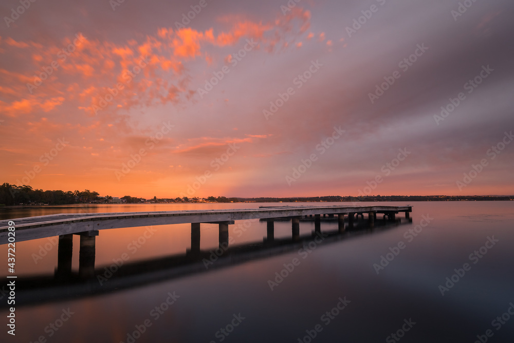 Colourful sunset reflections in a lake with a jetty stretching off into the distance on the coast of Australia. Colourful sunset reflections in a lake with a jetty stretching off into the distance on the coast of Australia.