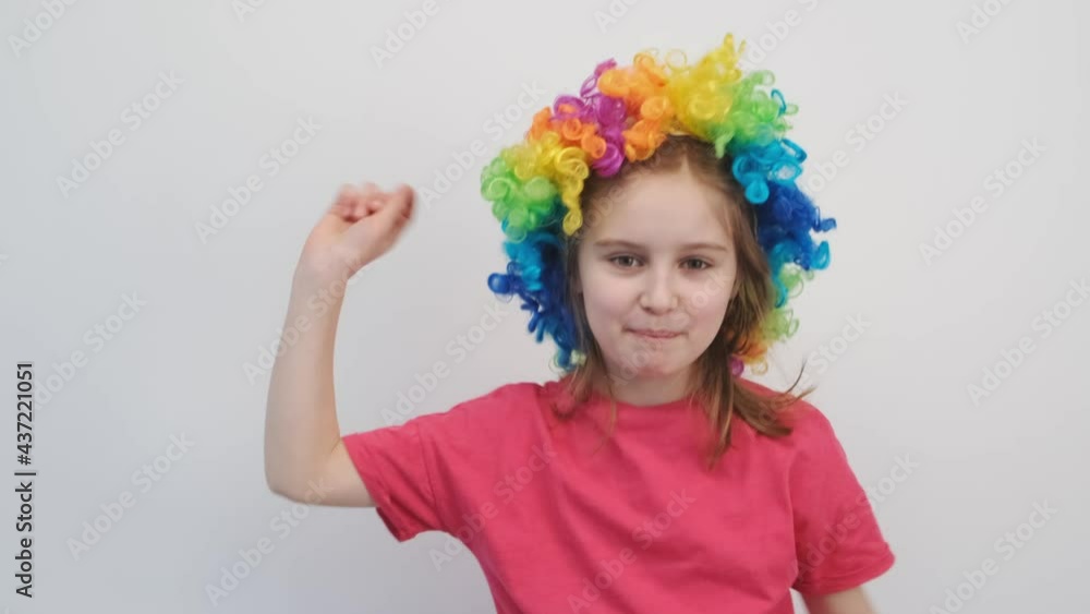Happy little girl in colorful wig singing and dancing near wall indoors Happy little girl in colorful wig singing and dancing near wall indoors