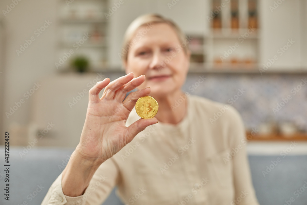 An elderly woman holds a bitcoin coin in her hand. Happy retirement life concept