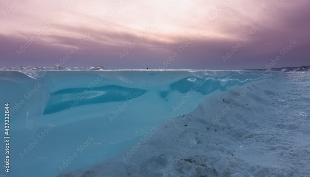 Turquoise ice floe against the pink sunset sky. Close-up. Side view. Snow and ice fragments on the surface of a frozen lake. Baikal