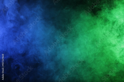 Artificial magic smoke in blue green light on black background