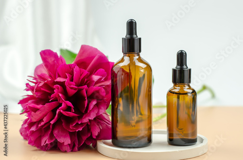 Two glass bottles with natural essential oils on a white podium with a peony flower. Cosmetic product on white geometric podium. Natural organic self care products