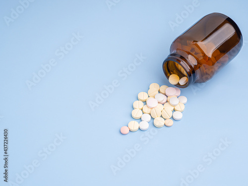 Close-up of tablets medicine spilling out of a drug bottle on a light blue background. Side view. Space for text. Medicine and treatment concept