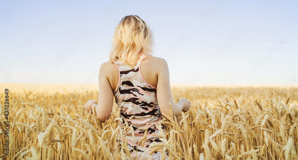 Young woman in a wheat field. Girl in dress walking through field and touches wheat. Rich Harvest concept. Banner with copy space. Young woman in a wheat field. Girl in dress walking through field and touches wheat. Rich Harvest concept. Banner with copy space.