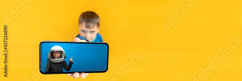 The child holds the phone in his hand for advertising on a yellow background. Color © vovan