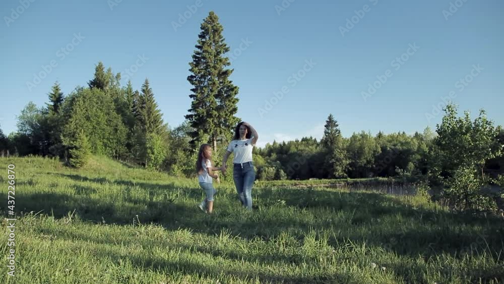 Happy mom and daughter are walking on the shore of the lake in the summer in a clearing among the trees