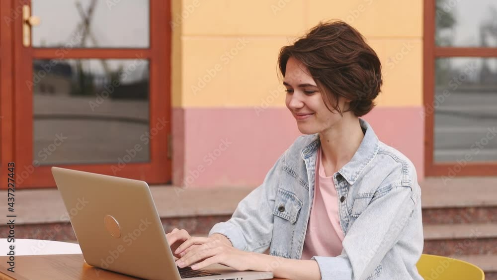 Young woman 20s wears denim shirt pink t-shirt user work on laptop pc computer sit in street cafe rest relax spring city sunshine day nature outdoors Mobile office freelance business lifestyle concept Young woman 20s wears denim shirt pink t-shirt user work on laptop pc computer sit in street cafe rest relax spring city sunshine day nature outdoors Mobile office freelance business lifestyle concept