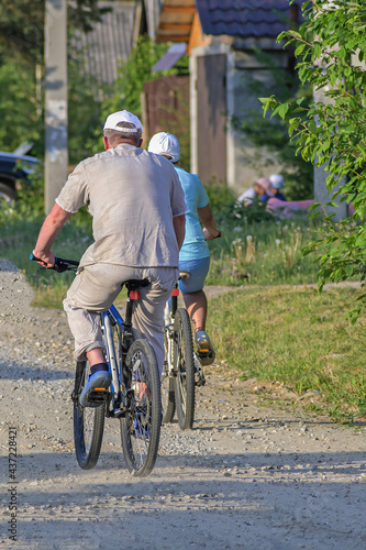 A man and a woman ride bicycles on a rural street on a summer day