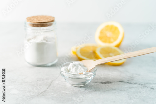 Eco friendly natural cleaners, jar with baking soda, lemon and wooden spoon on marble table background. Organic ingredients for homemade cleaning. Zero waste concept.