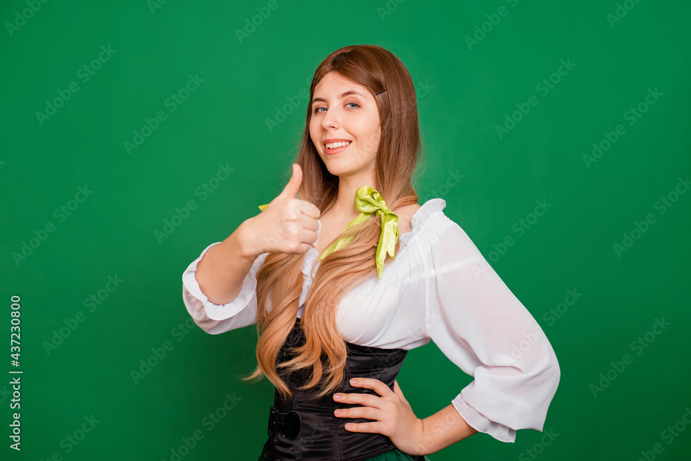 Young woman showing thumb up gesture and smiling isolated on green background. St. Patrick's Day and Oktoberfest celebration concept.