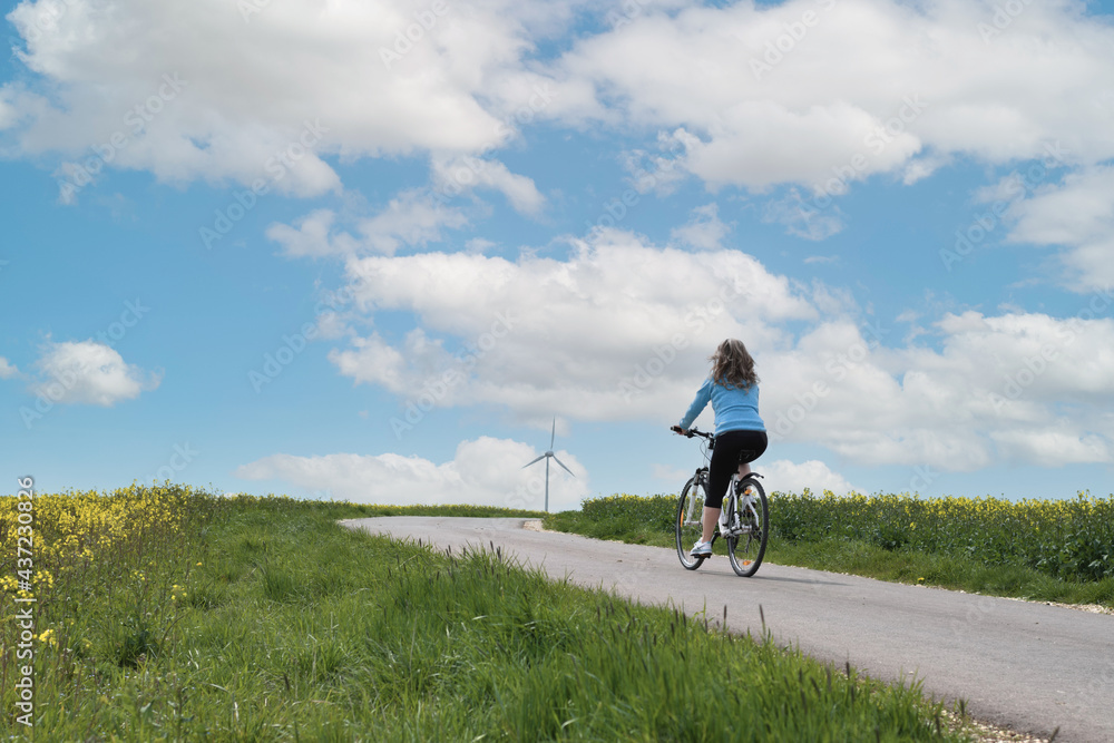 Rear view of a woman riding a bycicle  in the field .Wind turbine in the background