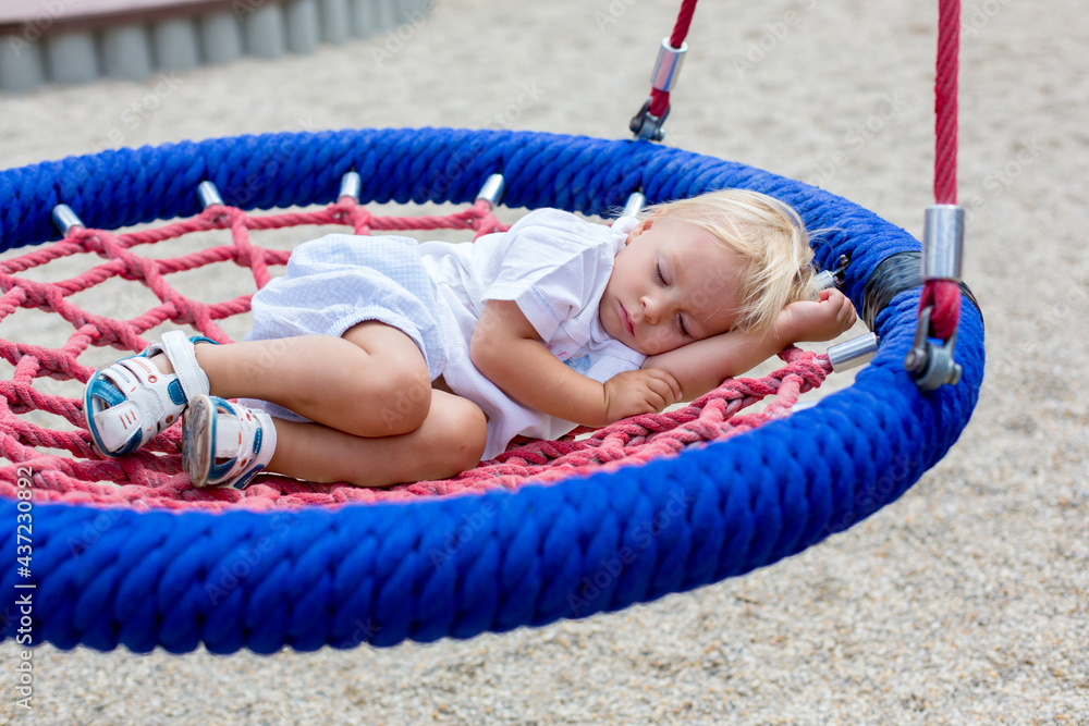 Little toddler boy, sleeping in a round swing on a playground, tired after full day of games Little toddler boy, sleeping in a round swing on a playground, tired after full day of games