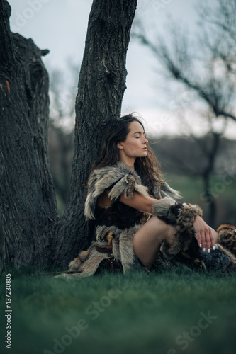 Woman rests under tree on grass in image of warrior amazon. photo