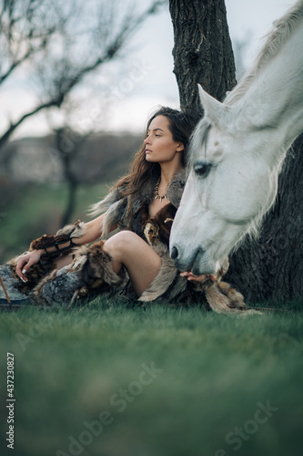 Woman in image of warrior amazon rests under tree near her horse. © Stanislav