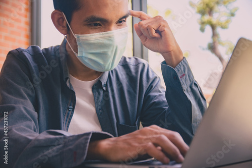 Asian man wear face mask protect covid19 coronavirus. Man use laptop computer working in coffee cafe
