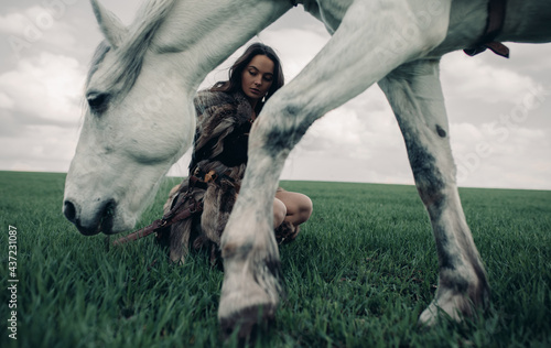 Woman sits on meadow in image of warrior amazon near grazing horse.
