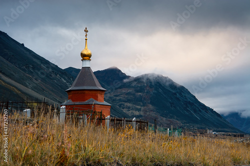 A small Orthodox chapel in a cemetery in the tundra among the mountains in the Far North of Russia in the Arctic. Gloomy autumn arctic landscape. Egvekinot, Chukotka, Siberia, Russia. Polar region. photo