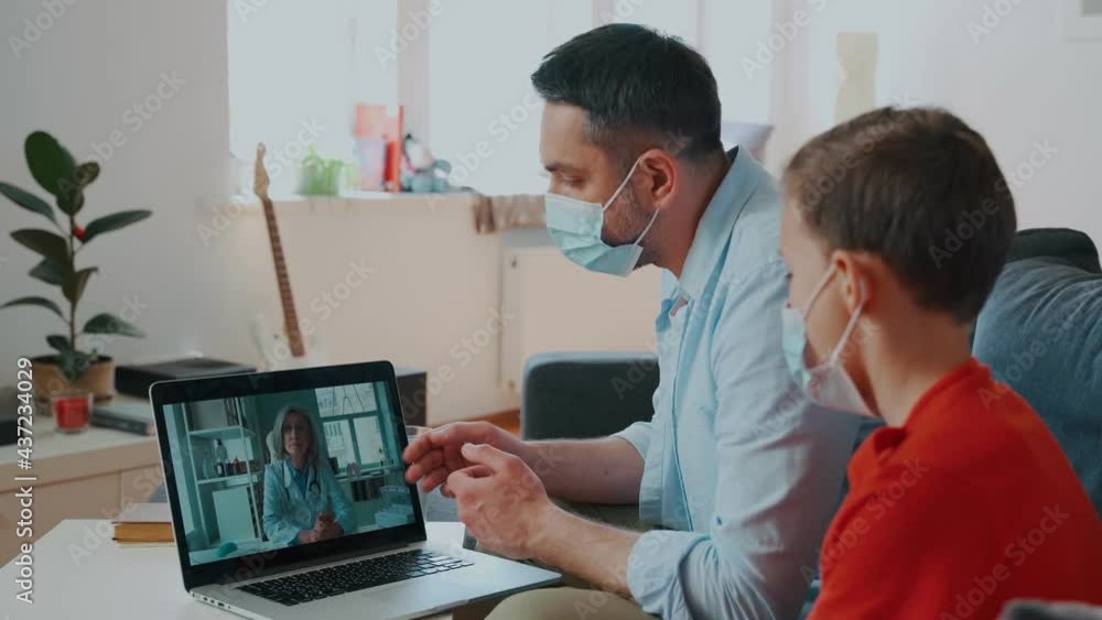 Father and son sitting on the couch and looking at laptop while having a video call with doctor Father and son sitting on the couch and looking at laptop while having a video call with doctor