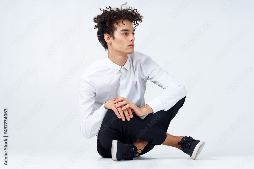 a guy in trousers in sneakers and a shirt sits on the floor and gestures with his hands in full growth a guy in trousers in sneakers and a shirt sits on the floor and gestures with his hands in full growth