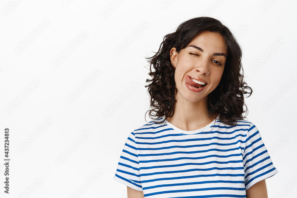 Emotions and people concept. Happy brunette girl showing tongue, winking and smiling happy, positive attitude and joyful emotions, standing over white background Emotions and people concept. Happy brunette girl showing tongue, winking and smiling happy, positive attitude and joyful emotions, standing over white background