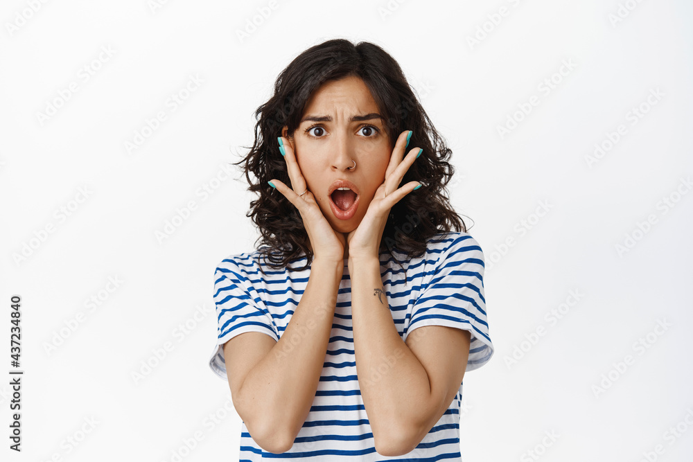 Shocked and alarmed young brunette woman, look startled at something awful terrible, scream from cringe and dislike, react at something bad and disgusting, shocking scene, white background
