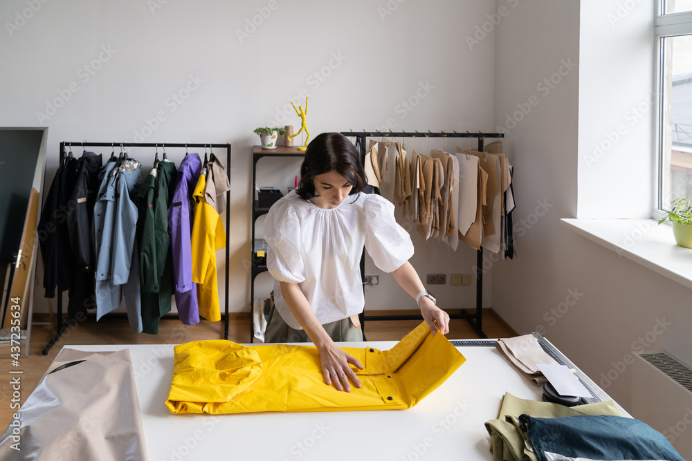 Clothes designer female wrapping new raincoat from trendy collection after  bespoke sewing in small atelier studio. Woman dressmaker entrepreneur or  freelance sewer seamstress at work in workshop space Stock-Foto | Adobe  Stock