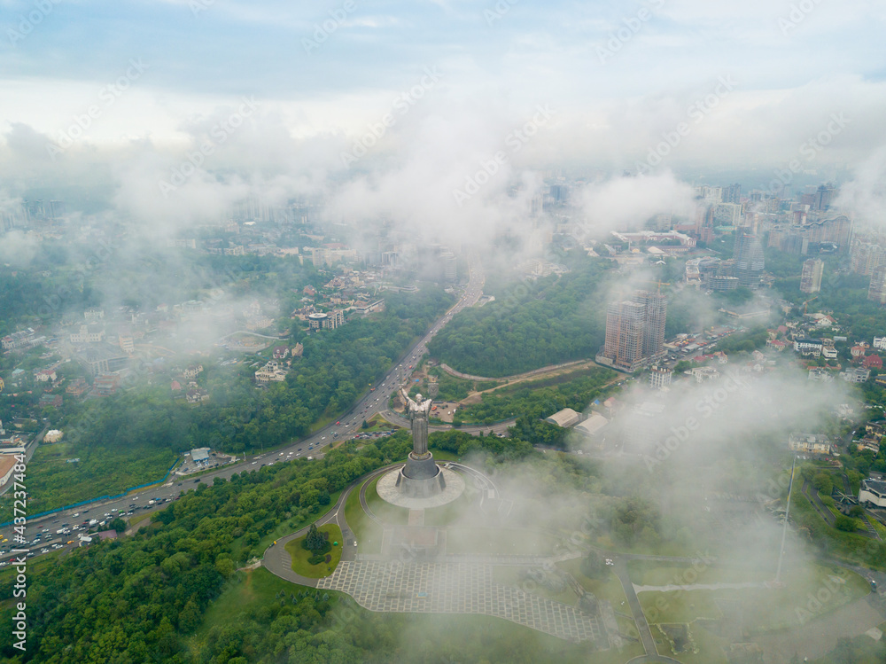 Fototapeta premium Motherland monument in Kiev between the clouds. Aerial drone view.