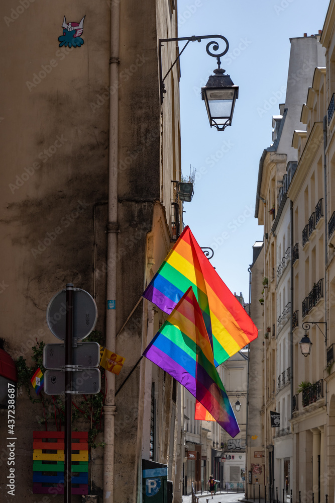 Lgbtq flags hanging at historic building corner during Paris pride. LGBTQIA culture symbol. Vintage lantern streetlight and bright gay flags waving in wind at sunny day in Paris, France