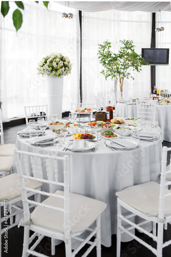 
Beautifully set table in the banquet hall of the restaurant. A table with appetizers for wine, cold dishes and salads. White tablecloths and napkins