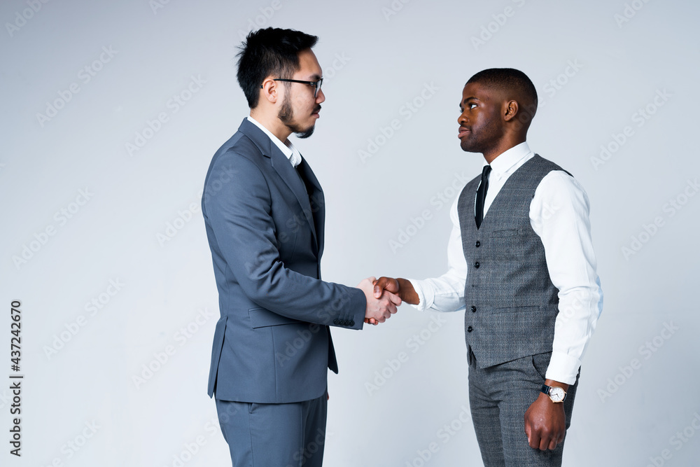African American man shakes hands with Asian businessman finishing negotiations. Isolated on gray background. African American man shakes hands with Asian businessman finishing negotiations. Isolated on gray background.