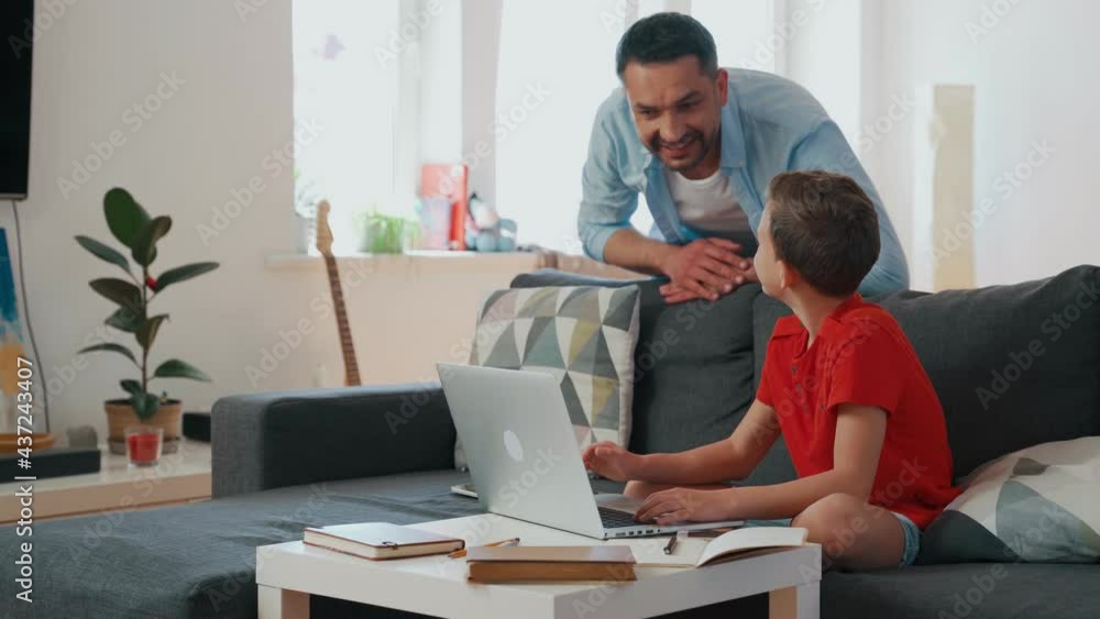 Father helping his son with homework while sitting on the couch in the living room Father helping his son with homework while sitting on the couch in the living room