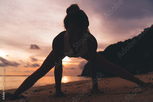 Female doing Tadasana while practising yoga on beach at sunset photo