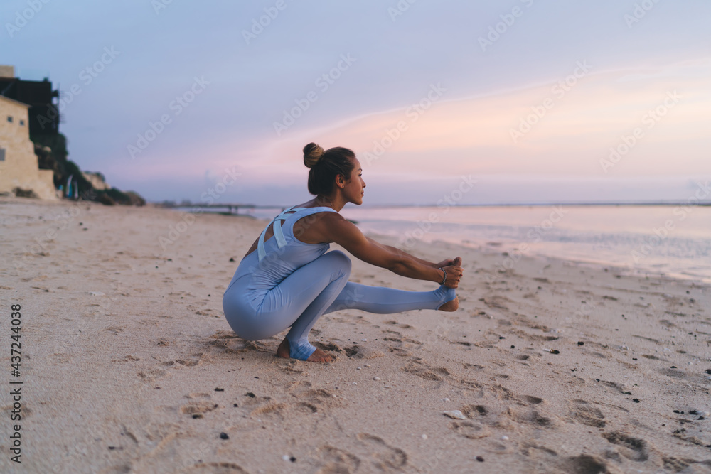 Motivated woman in tracksuit practice stretching yoga pose breathing and enjoying recreation at oceania coastline, female trainer feeling inspiration and balance in asana keeping body shape