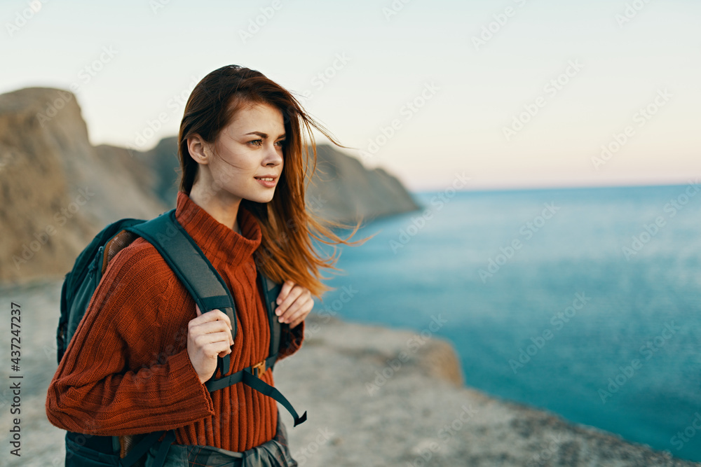 beautiful woman in a sweater with a backpack on her back near the sea in the mountains in nature beautiful woman in a sweater with a backpack on her back near the sea in the mountains in nature
