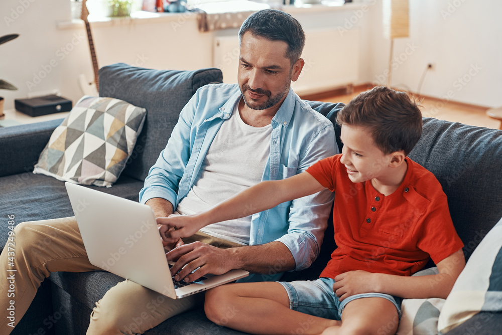 Father and son using laptop and smiling while spending time at home Father and son using laptop and smiling while spending time at home