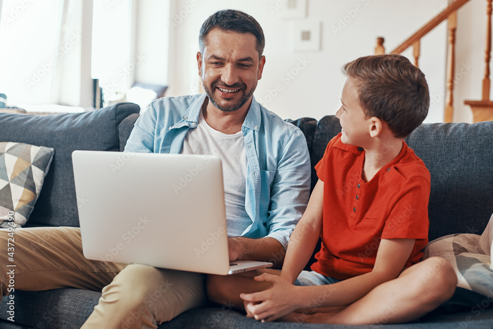 Father and son using laptop and smiling while spending time at home