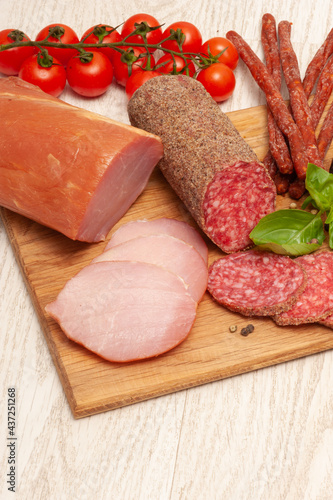Different types of sausages with tomatoes and herbs on a wooden board. Top view