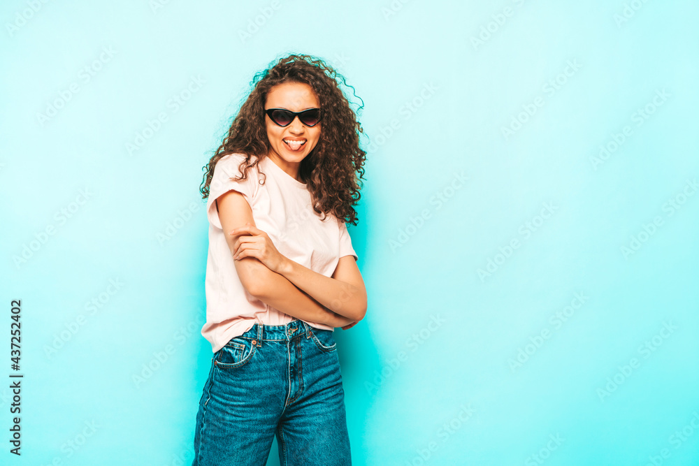 Beautiful black woman with afro curls hairstyle.Smiling model in white trendy jeans clothes. Sexy carefree female posing near blue wall in studio. Tanned and cheerful Beautiful black woman with afro curls hairstyle.Smiling model in white trendy jeans clothes. Sexy carefree female posing near blue wall in studio. Tanned and cheerful
